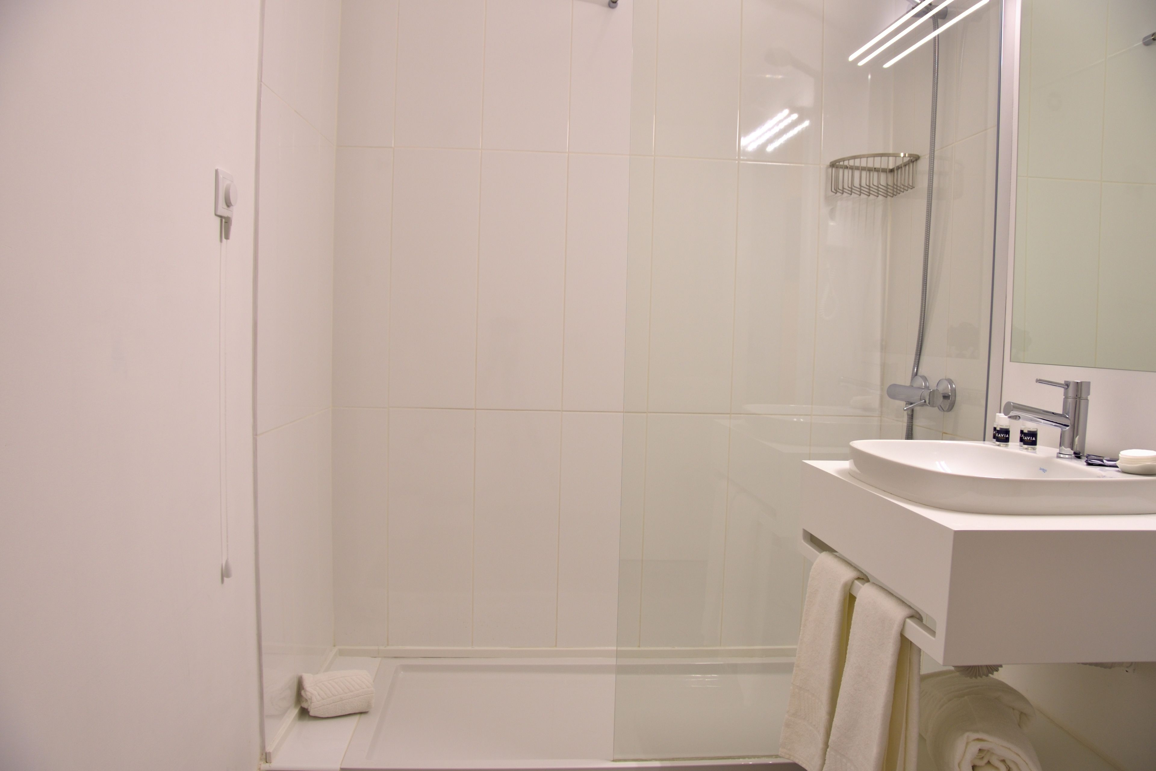 Un baño moderno con ducha de vidrio, lavamanos blanco y un espejo grande.