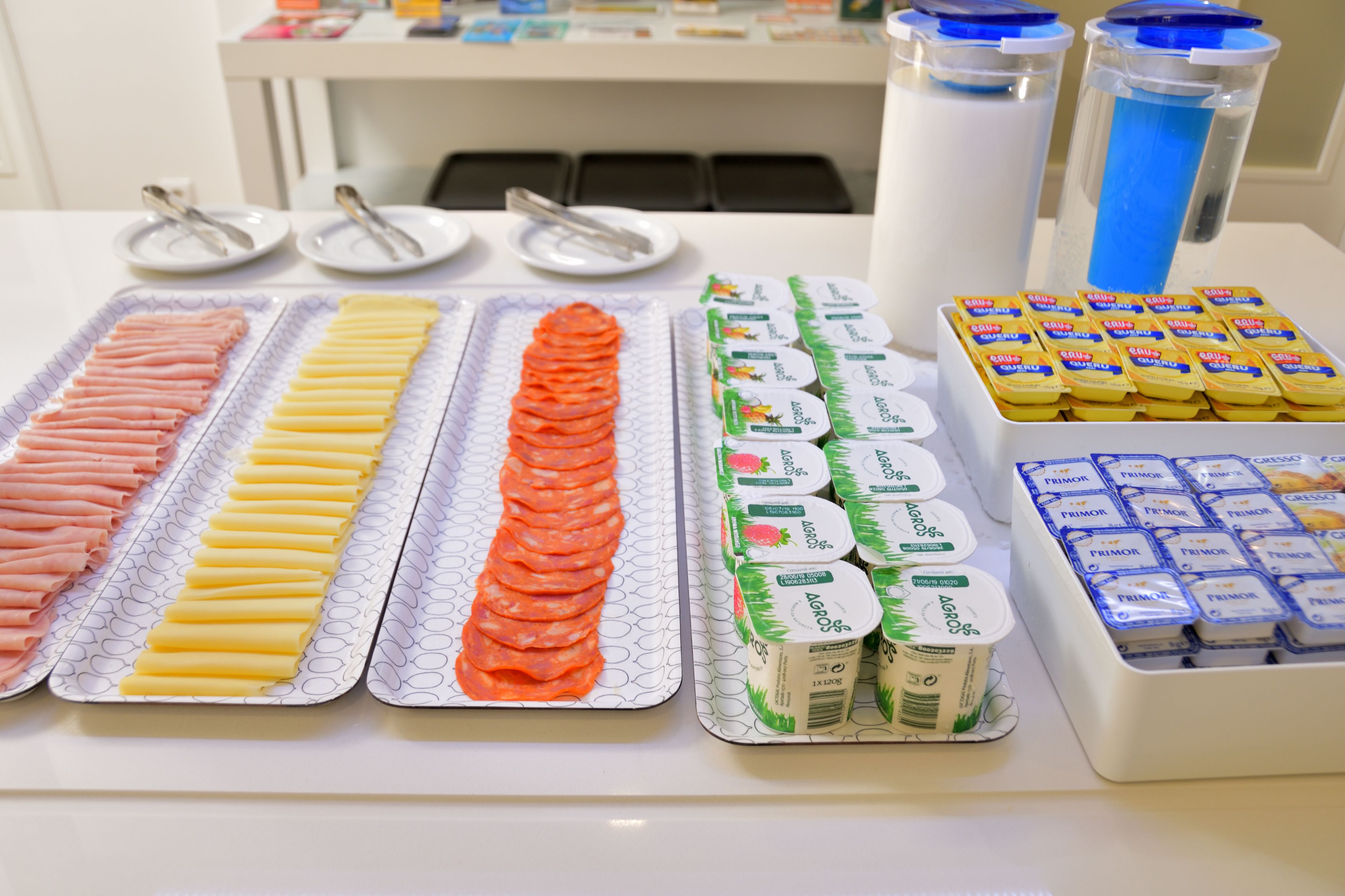 Una mesa de buffet con diferentes opciones de comida, incluyendo carnes en rodajas, quesos y recipientes de yogur.