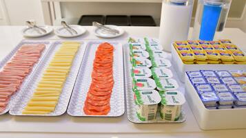 Una mesa de buffet con diferentes opciones de comida, incluyendo carnes en rodajas, quesos y recipientes de yogur.