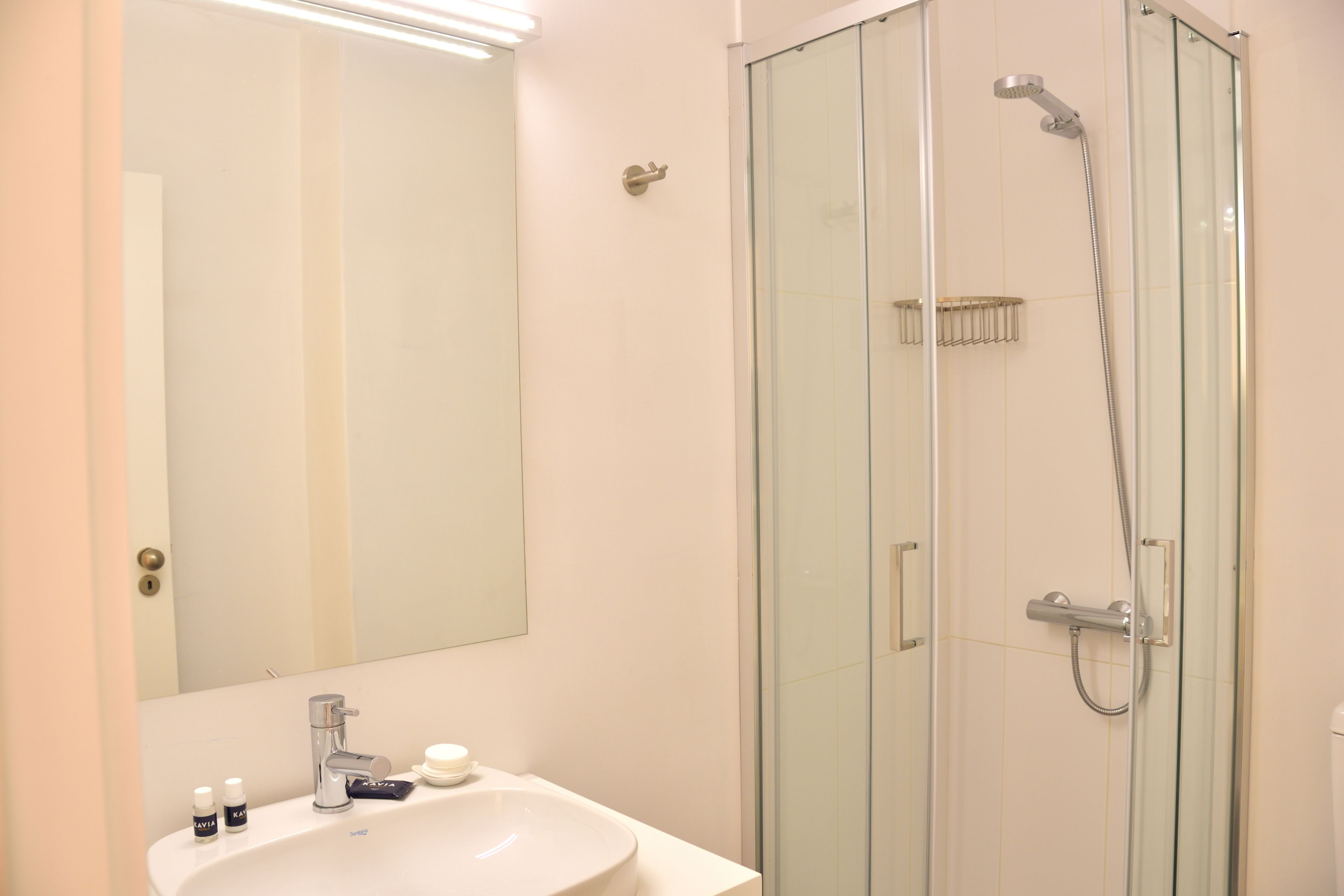 Un baño con ducha de vidrio, un lavamanos con espejo y artículos de tocador sobre el mostrador.