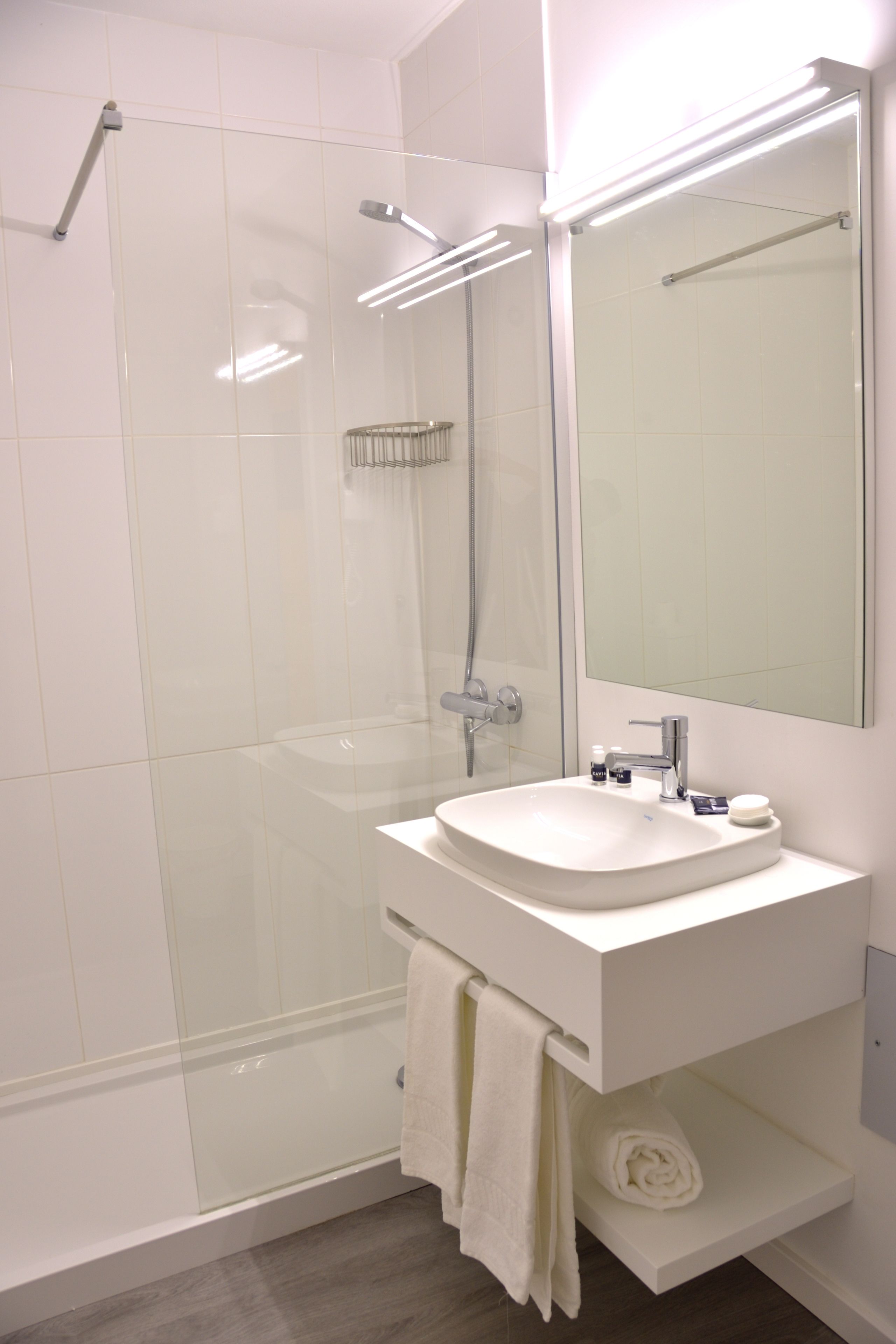 Een moderne badkamer met een douche in een glazen cabine, een witte wastafel en een grote spiegel.