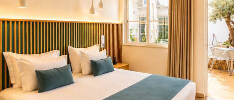 A modern hotel room with a large bed, bedside tables, a window with curtains, and a view of the outdoors.