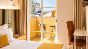 Habitación de hotel con cama, escritorio, silla, televisor y balcón con vistas a edificios.