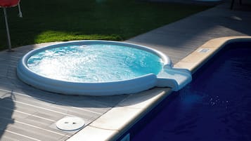 Een zwembad met een jacuzzi, omgeven door een betegeld zonnedek en een gazon.