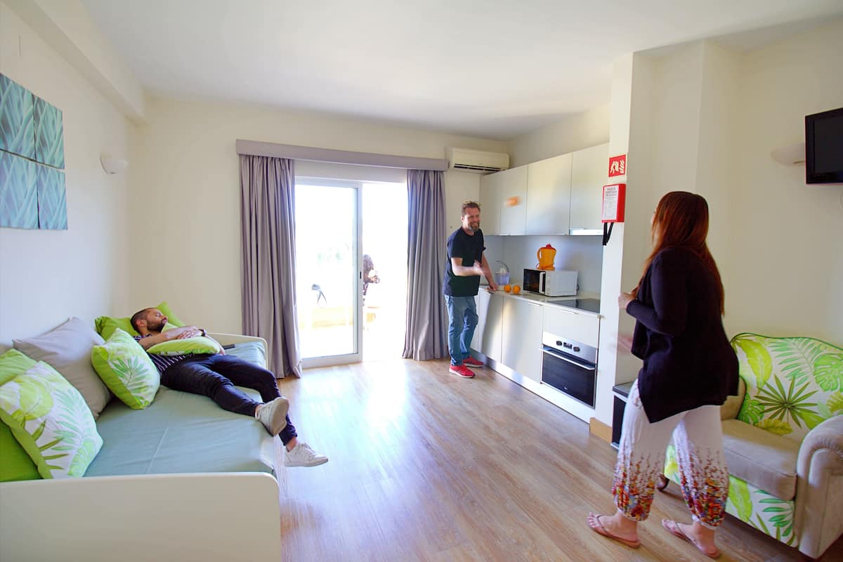 A modern living room with a sofa, a dining area with a table, and a kitchen with cabinets and appliances.