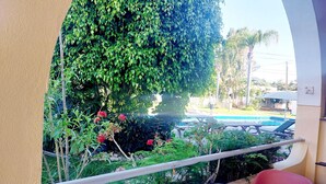 Ein Balkon mit Blick auf einen Swimmingpool, umgeben von üppiger Vegetation und Topfpflanzen.
