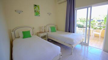 Une chambre d’hôtel avec deux lits simples, une petite table, une table de chevet et une porte-fenêtre coulissante donnant sur un espace extérieur aménagé avec des chaises.
