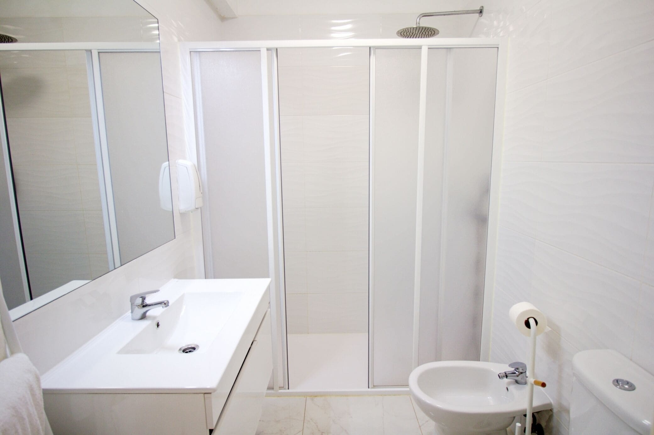 Un baño moderno con lavamanos blanco, espejo, inodoro y cabina de ducha.