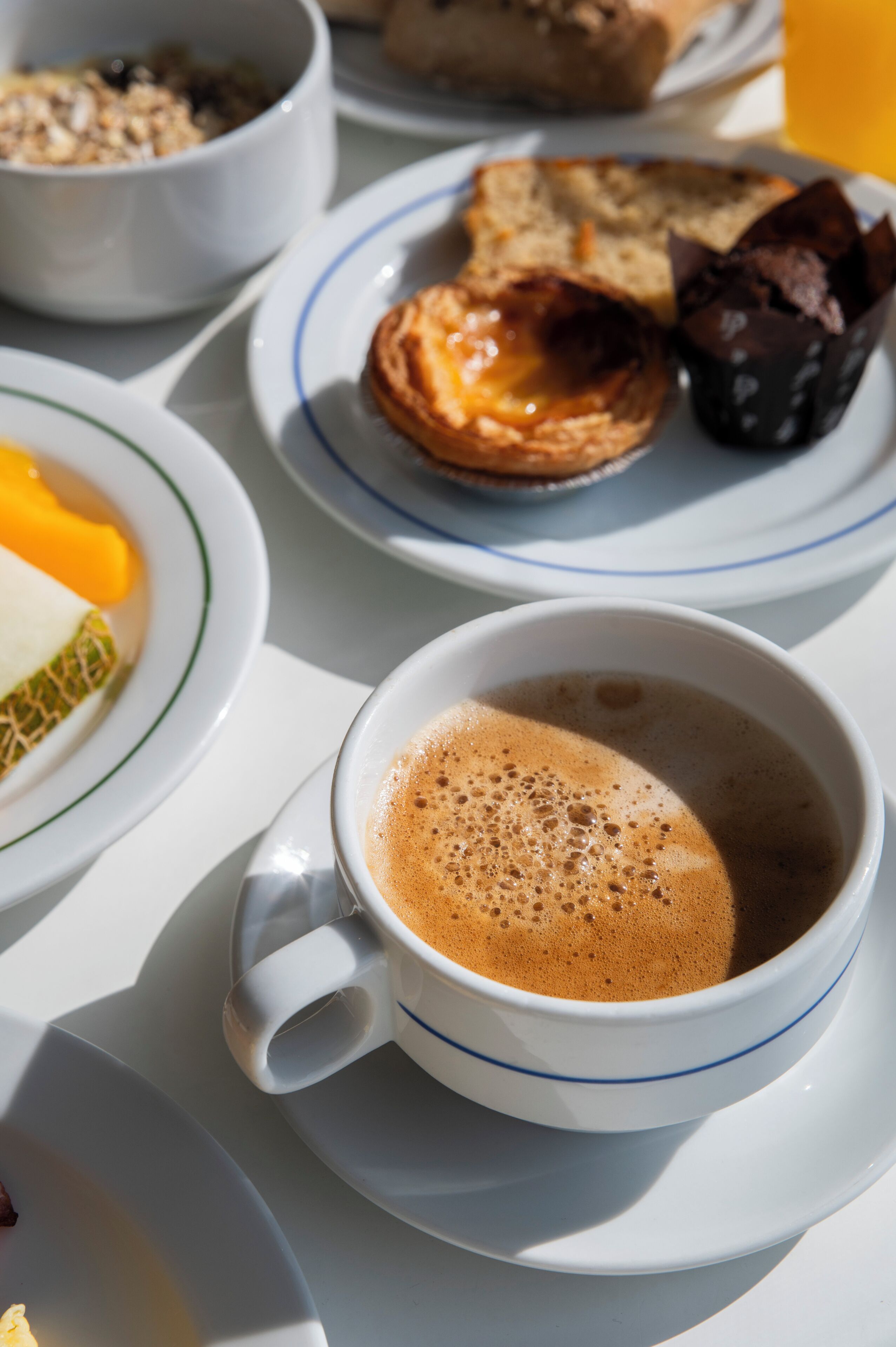 Une table mise pour le petit-déjeuner avec une tasse de café, une assiette de pain grillé et un muffin, et un bol de fruits.