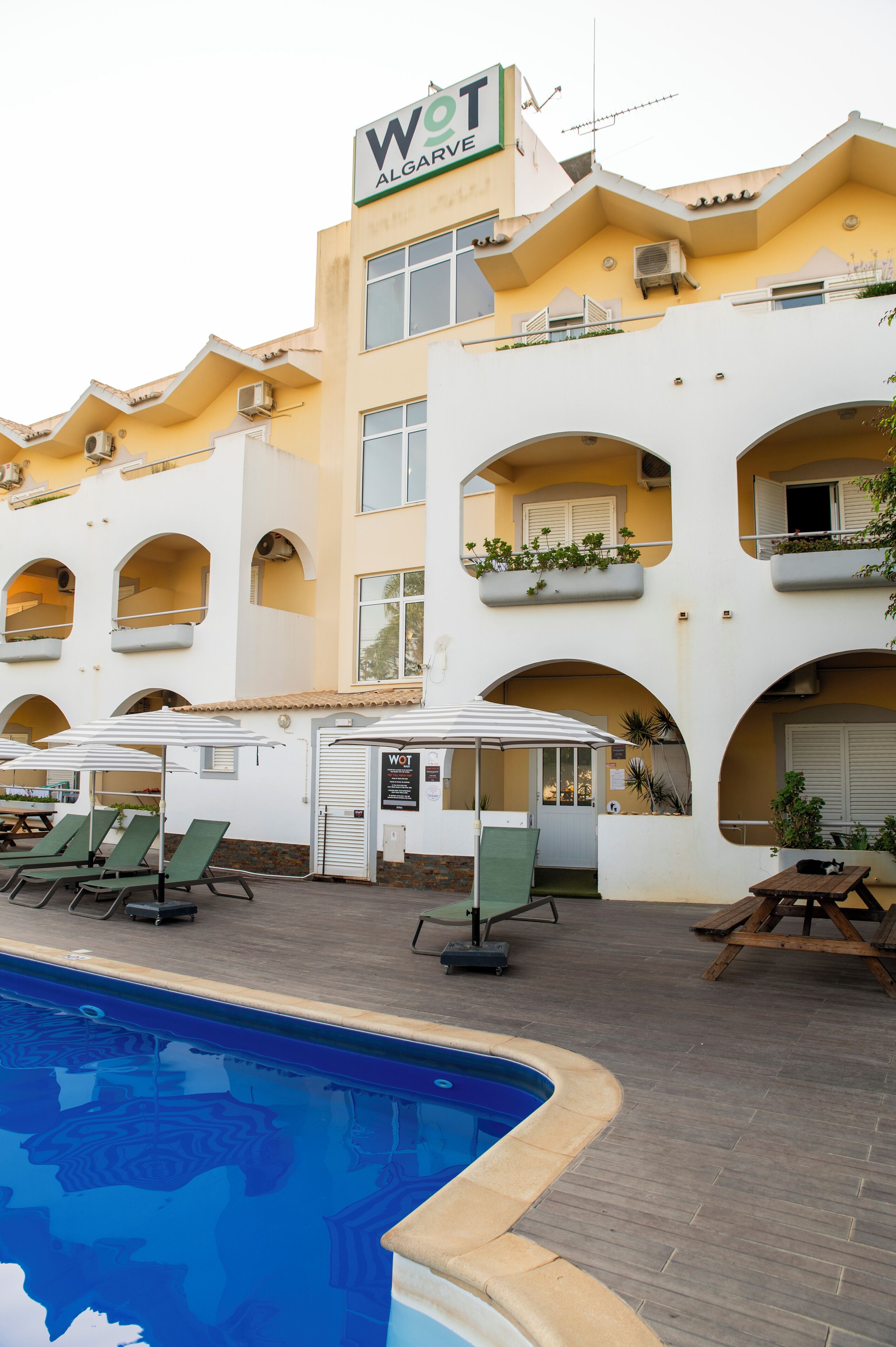 Um hotel com área de piscina, mobiliário de jardim e varandas com plantas.