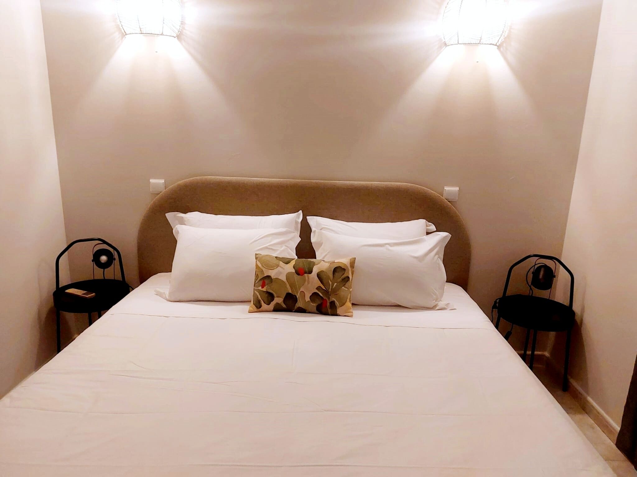 Ein ordentlich bezogenes Bett mit weißen Leinen und zwei Kissen, das von zwei schwarzen Sesseln mit Lampen eingerahmt wird.