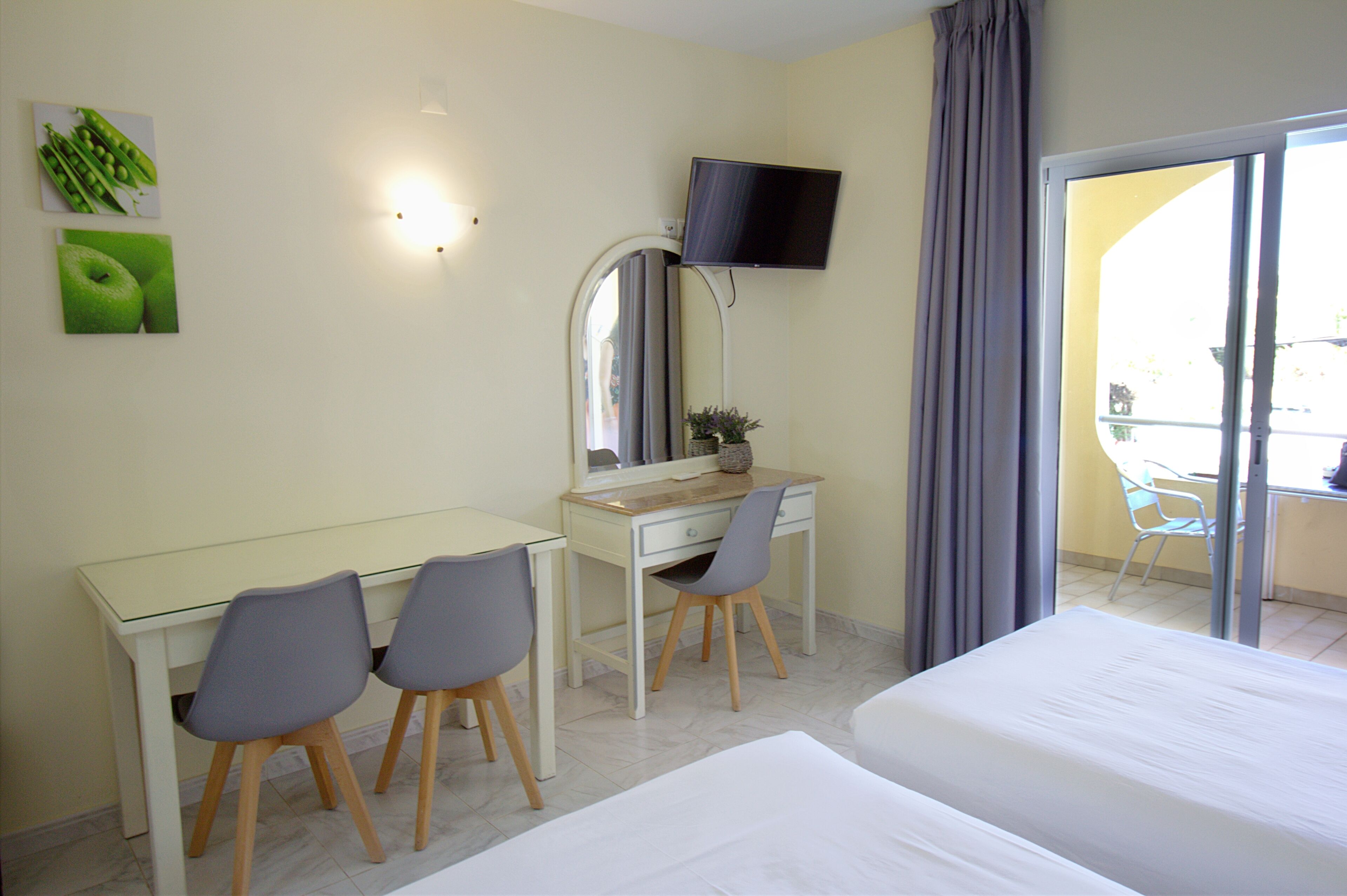 A hotel room with a bed, a desk with two chairs, a TV, and a balcony with a table and chairs.