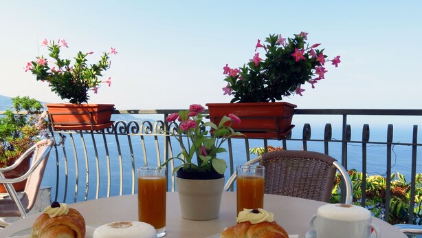 Una mesa dispuesta con cruasanes, tazas y un vaso de zumo de naranja, con vistas a un paisaje pintoresco.
