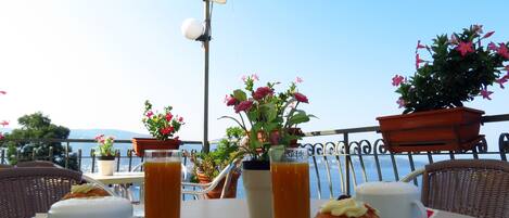 An outdoor dining area with a table set for two, featuring a croissant, a glass of orange juice, and a white cup.