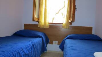 A room with two beds, a wooden headboard, a window with yellow curtains, and a light switch on the wall.