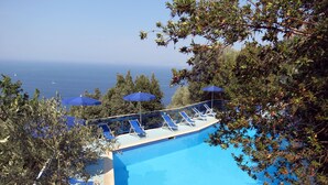 Zona de piscina con sillones de descanso y sombrillas, con vistas a una masa de agua.