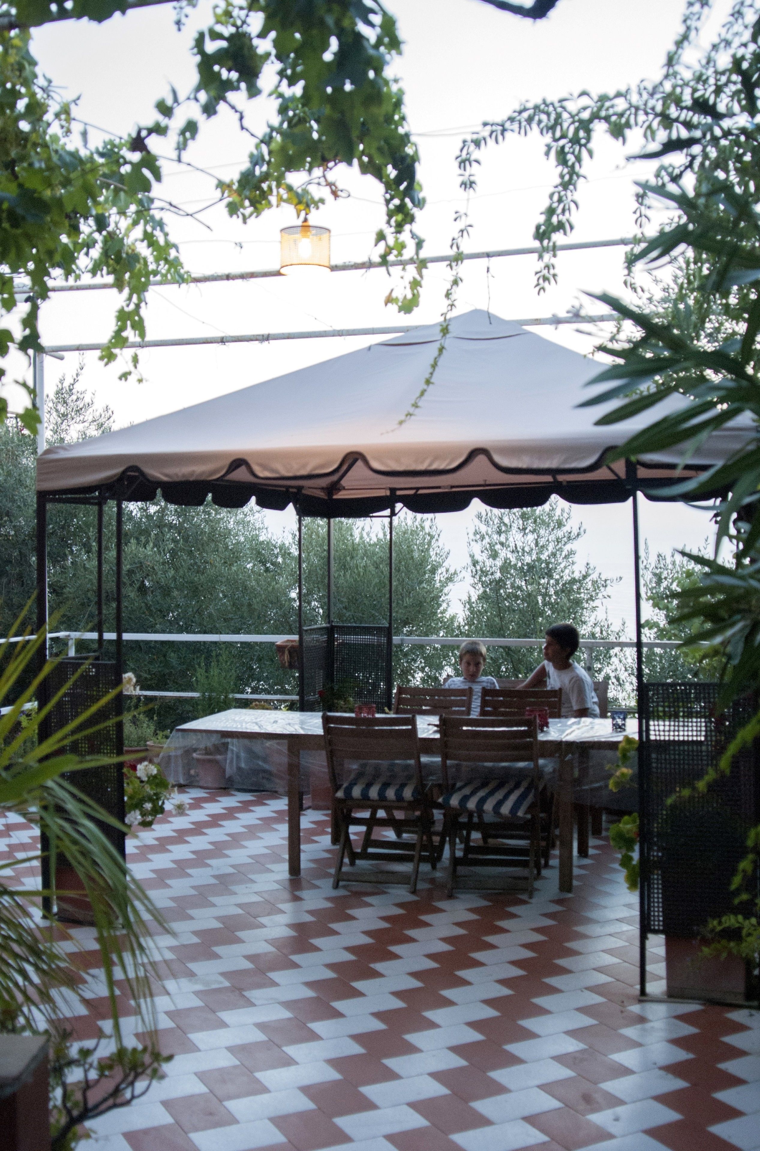 A covered patio area with a checkered floor, a table with chairs, and a canopy overhead.