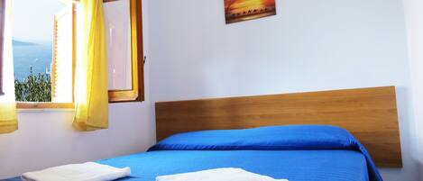 A bedroom with a wooden headboard, a blue bedspread, and a painting of a sunset.