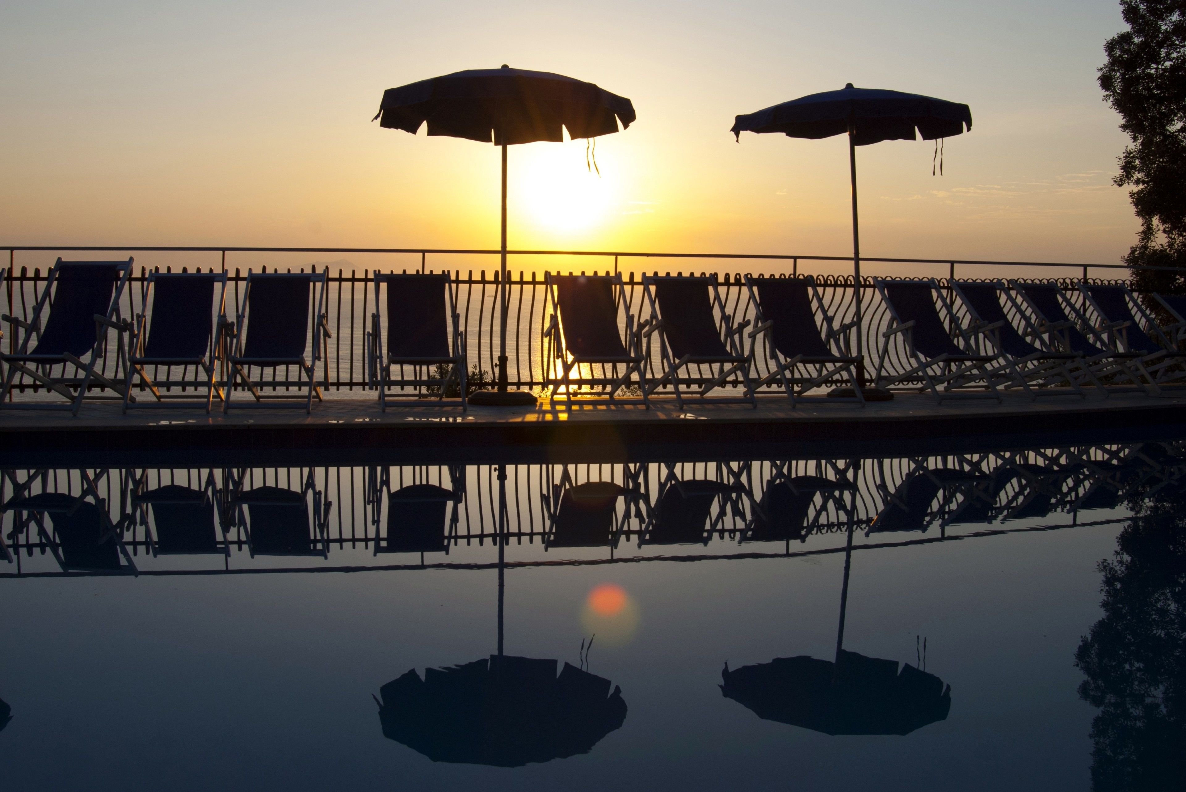 A poolside area with lounge chairs and umbrellas during sunset.