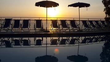 Un espace aménagé au bord de la piscine, avec des chaises longues et des parasols, au moment du coucher du soleil.
