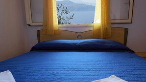 Una cama con un edredón azul, dos toallas blancas y una ventana con cortinas amarillas.