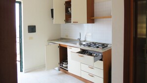 Cocina compacta con estufa a gas, pileta y alacenas de madera.