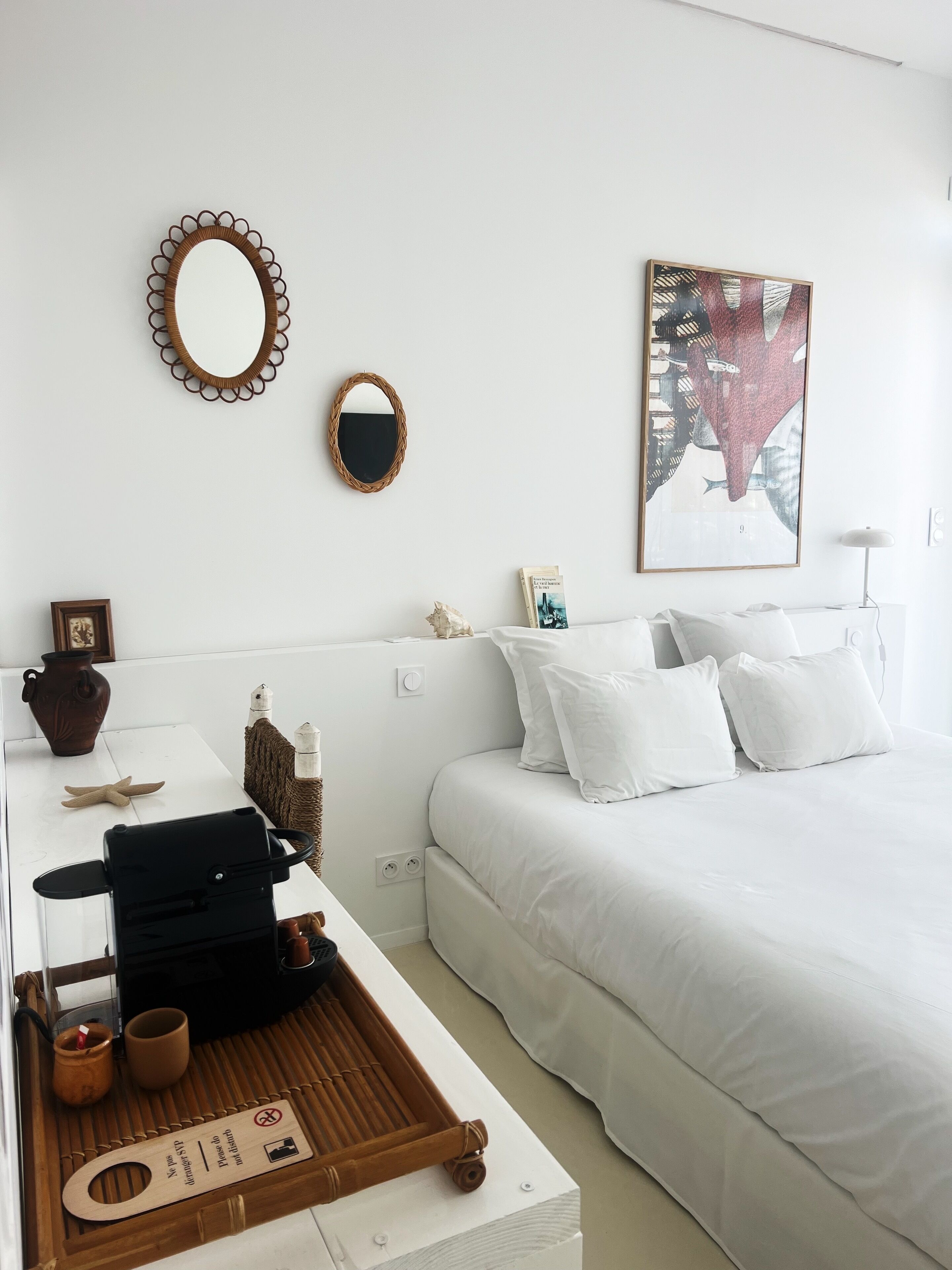 A neatly arranged bedroom with a bed, a bedside table with a tray, a mirror, and a framed picture on the wall.