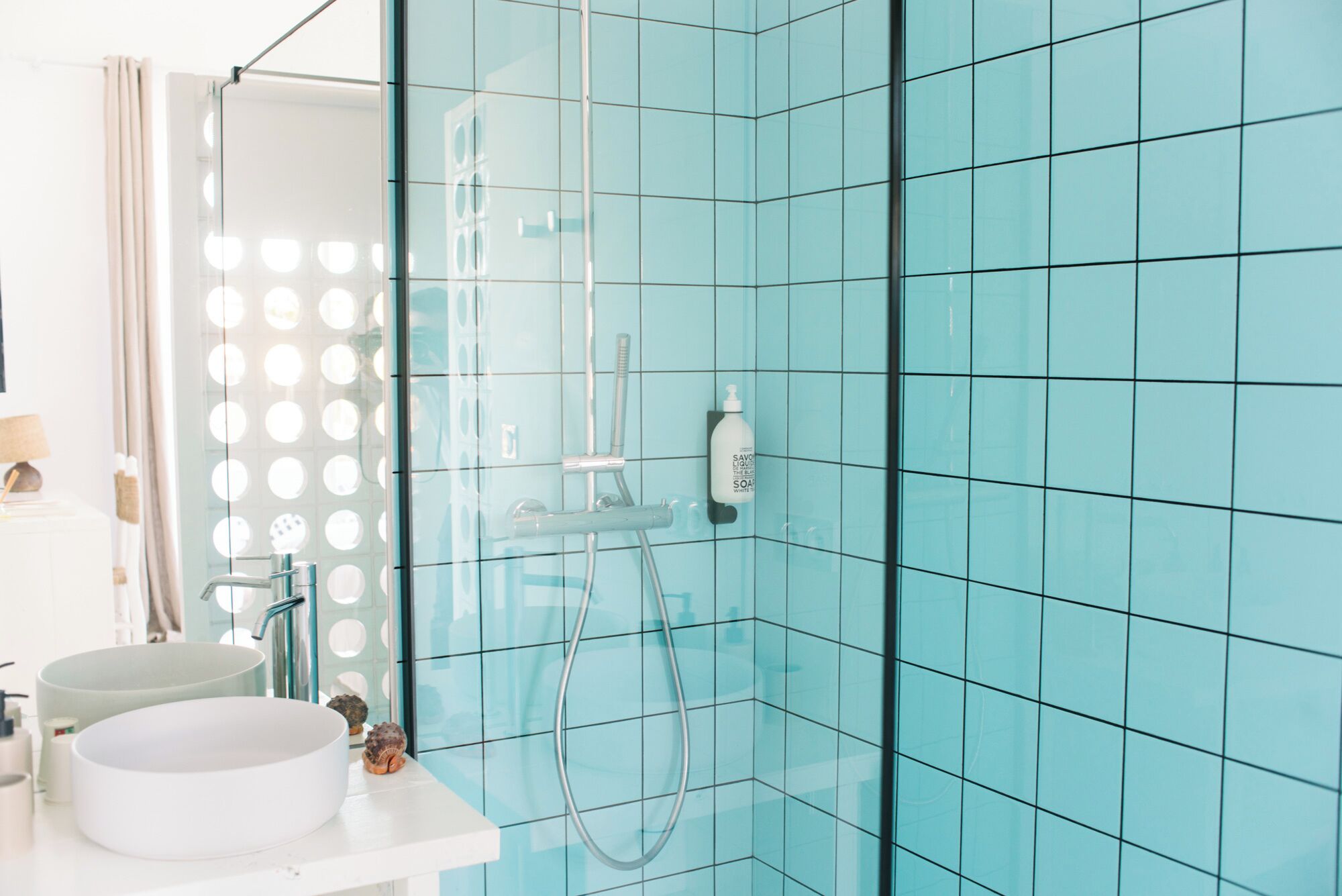 A bathroom with a glass shower enclosure, a white sink, and a mirror with lights.