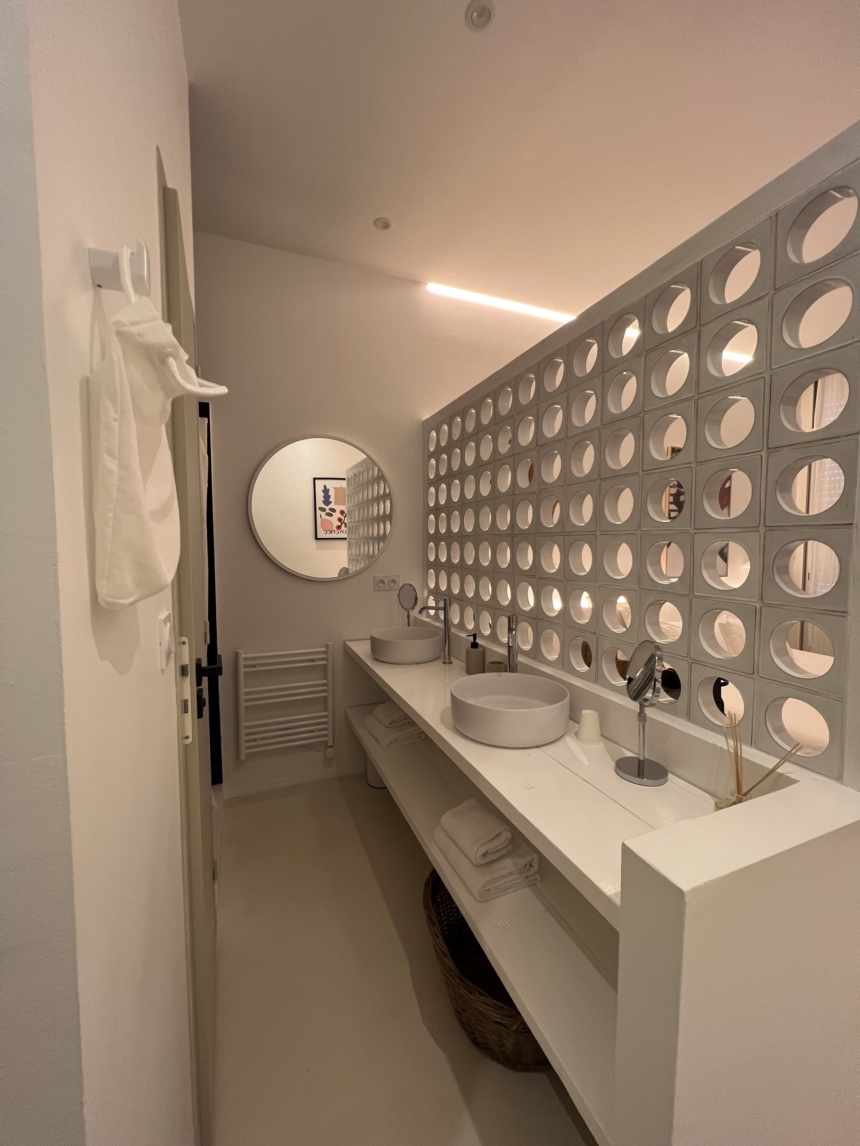 Un baño moderno con un tocador blanco, un espejo redondo y una pared decorativa con diseños circulares.