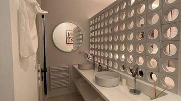 Un baño moderno con un tocador blanco, un espejo redondo y una pared decorativa con diseños circulares.