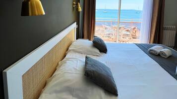 Habitación de hotel con una cama grande, vistas al mar y un balcón con sillas.