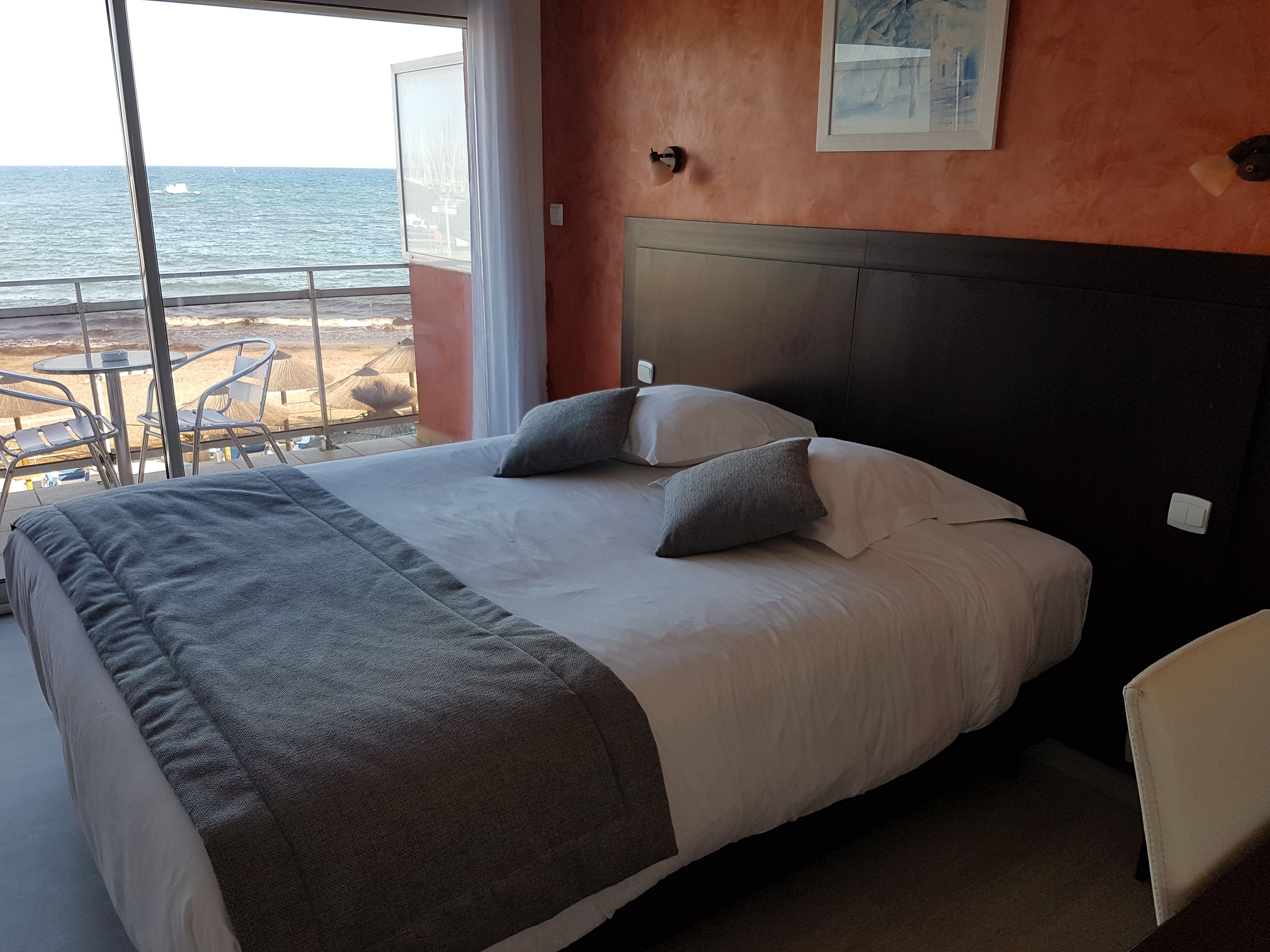 A hotel room with a large bed, a view of the sea, and a balcony with chairs.