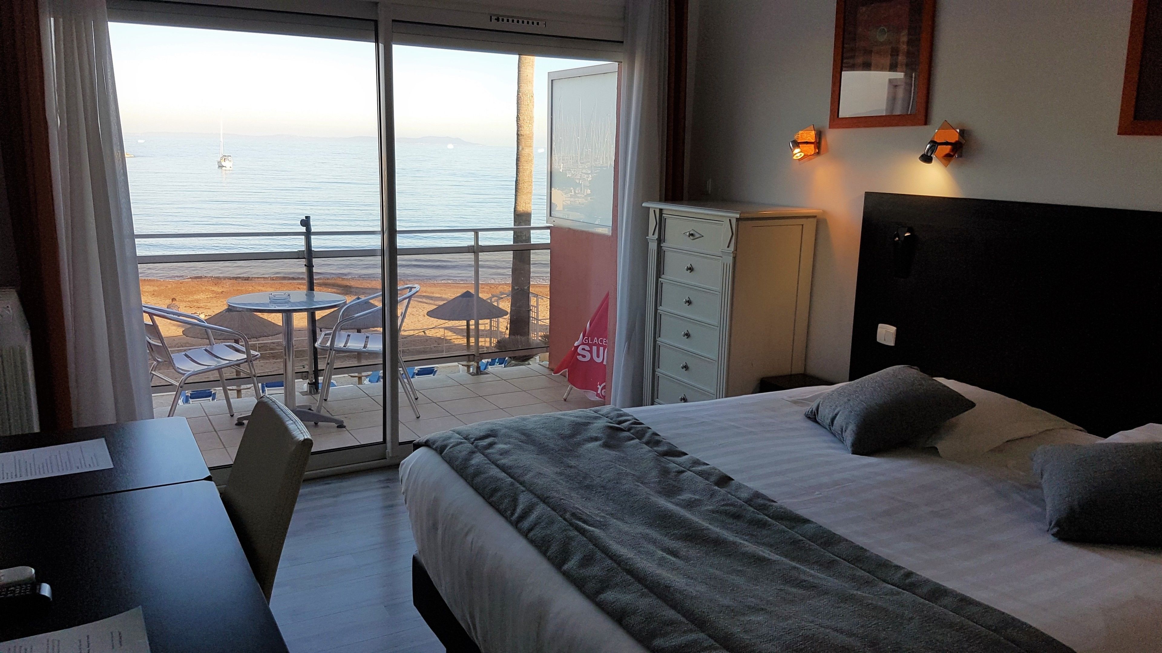 A hotel room with a bed, desk, and a view of the beach and ocean.