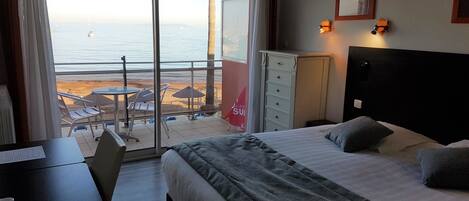 A hotel room with a bed, desk, and a view of the beach and ocean.