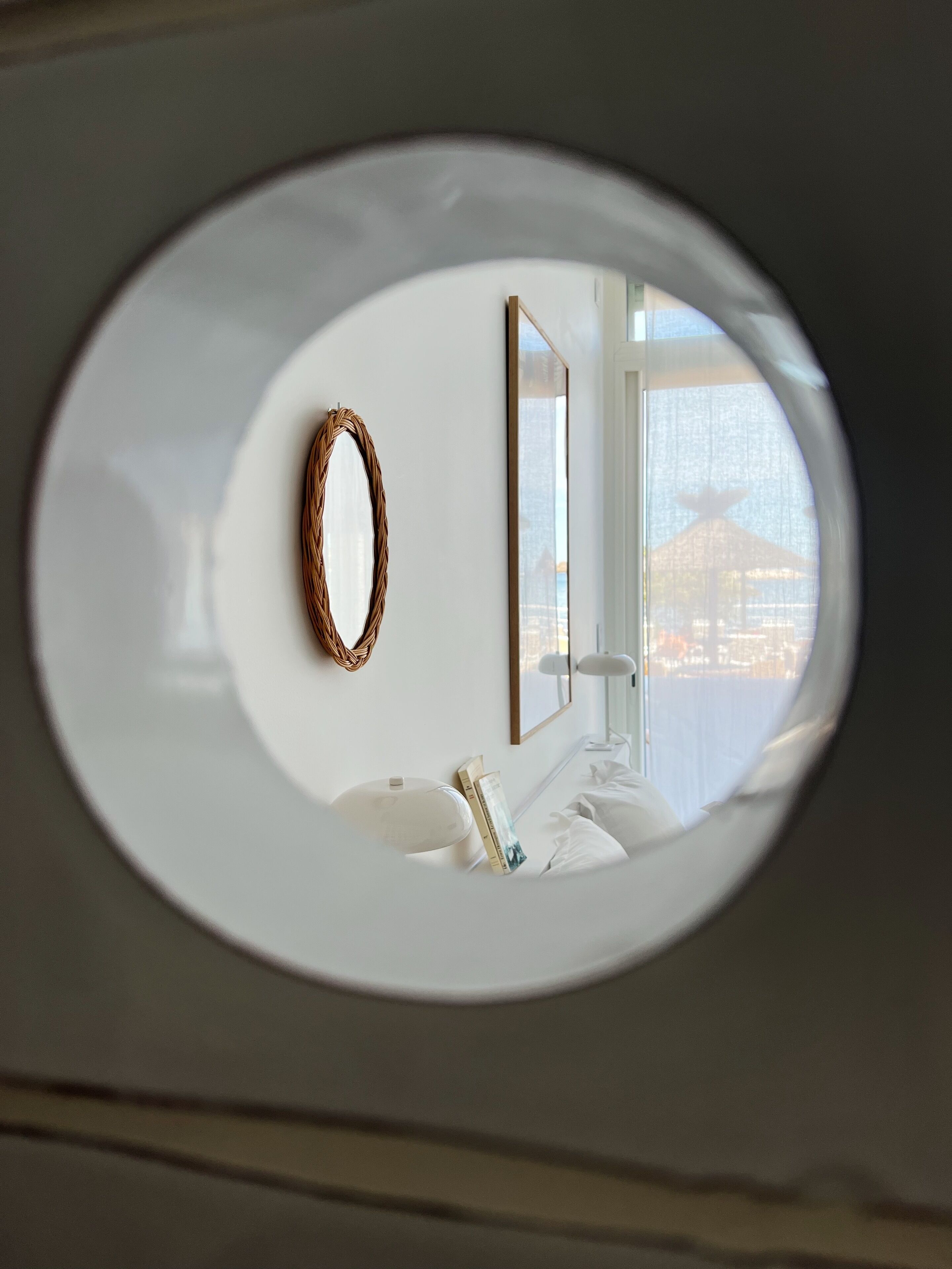 A room with a bed, a bedside table, a mirror, and a window with a view of a cityscape.