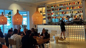 Un restaurante con barra, sillas de madera y lámparas de mimbre colgantes.