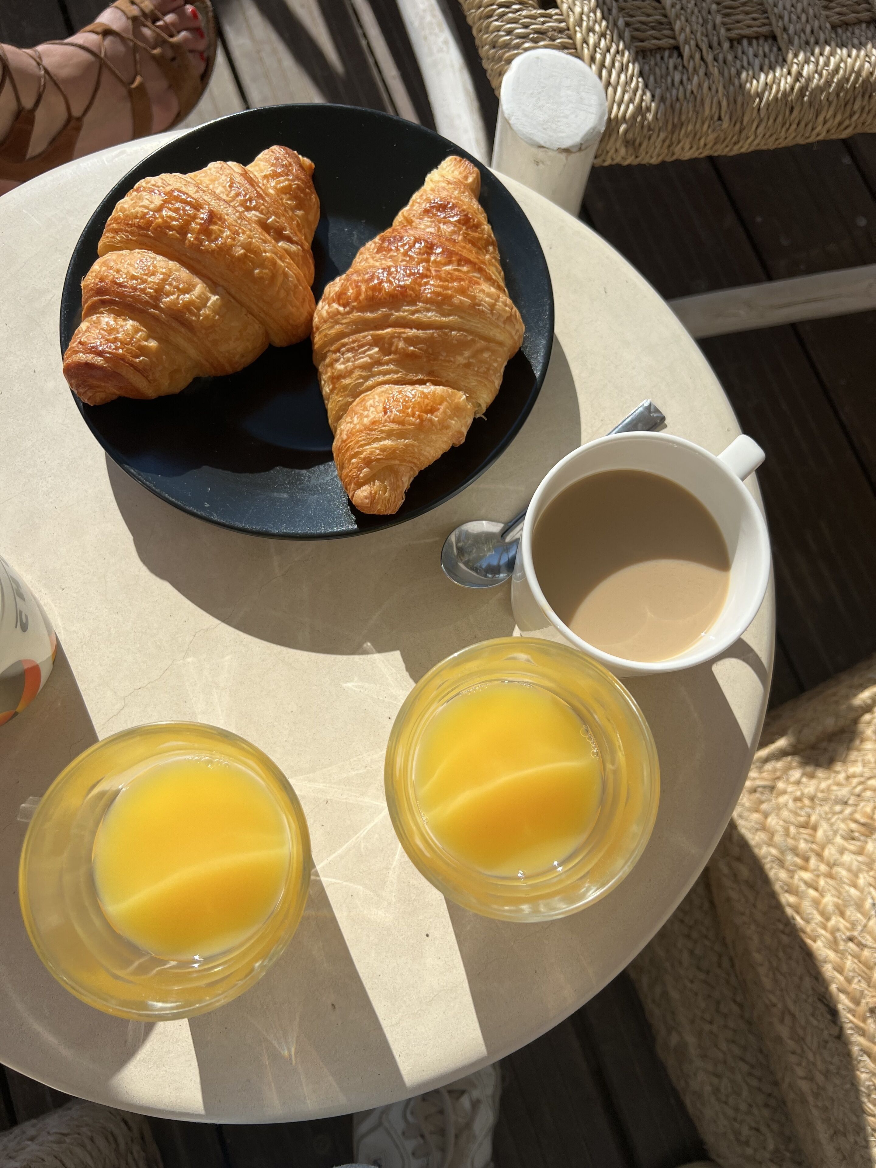 A round table with a plate of croissants, a cup of coffee, and two glasses of orange juice.