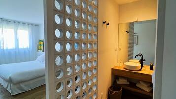 Ein modernes Hotelzimmer mit einem großen Bett, Holzboden, einem Badezimmer mit Waschbecken und Spiegel sowie einer Wand mit kreisförmigen Ausschnitten.