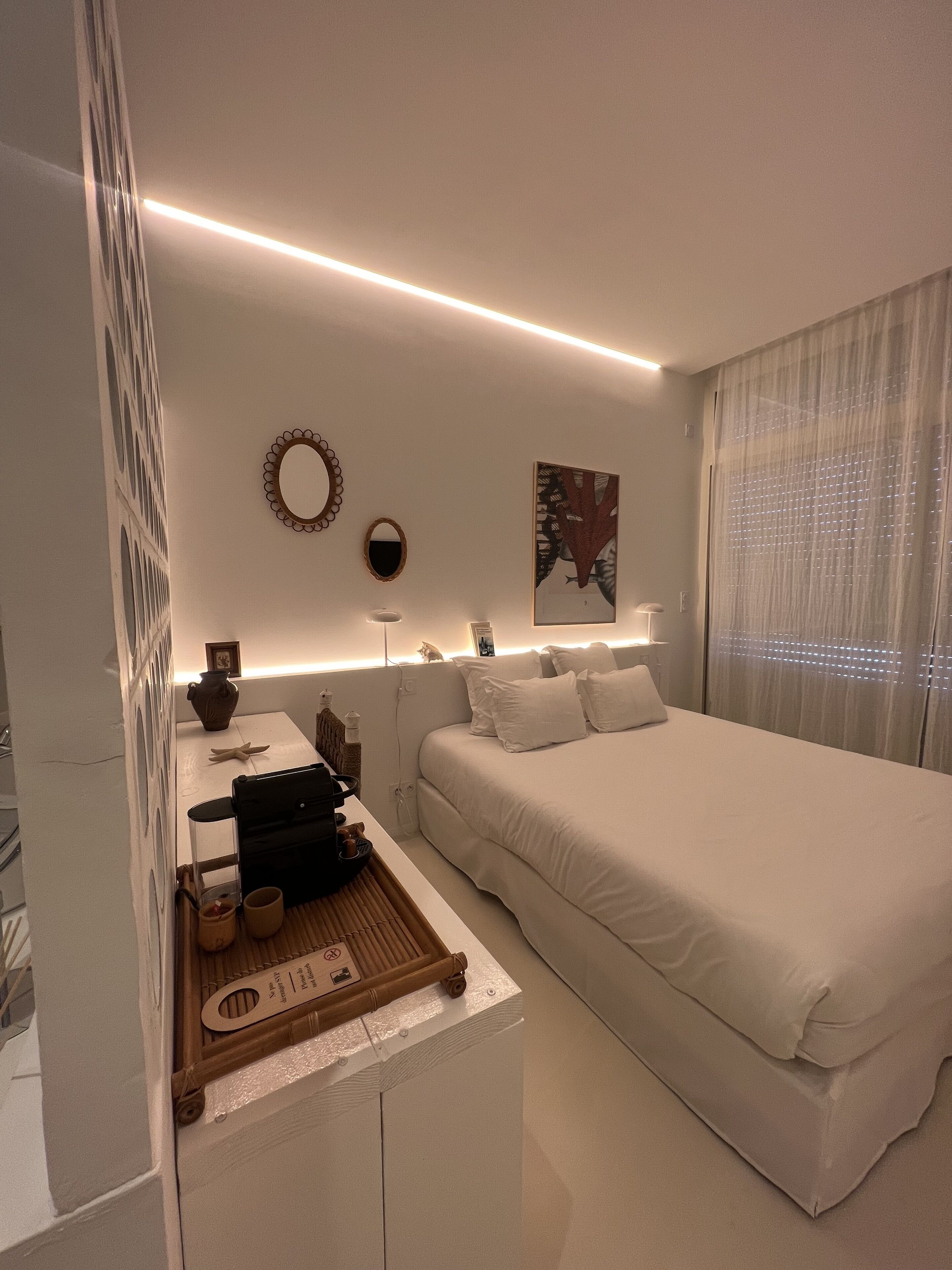 A modern bedroom with a large bed, bedside tables, a small desk, and a decorative mirror.