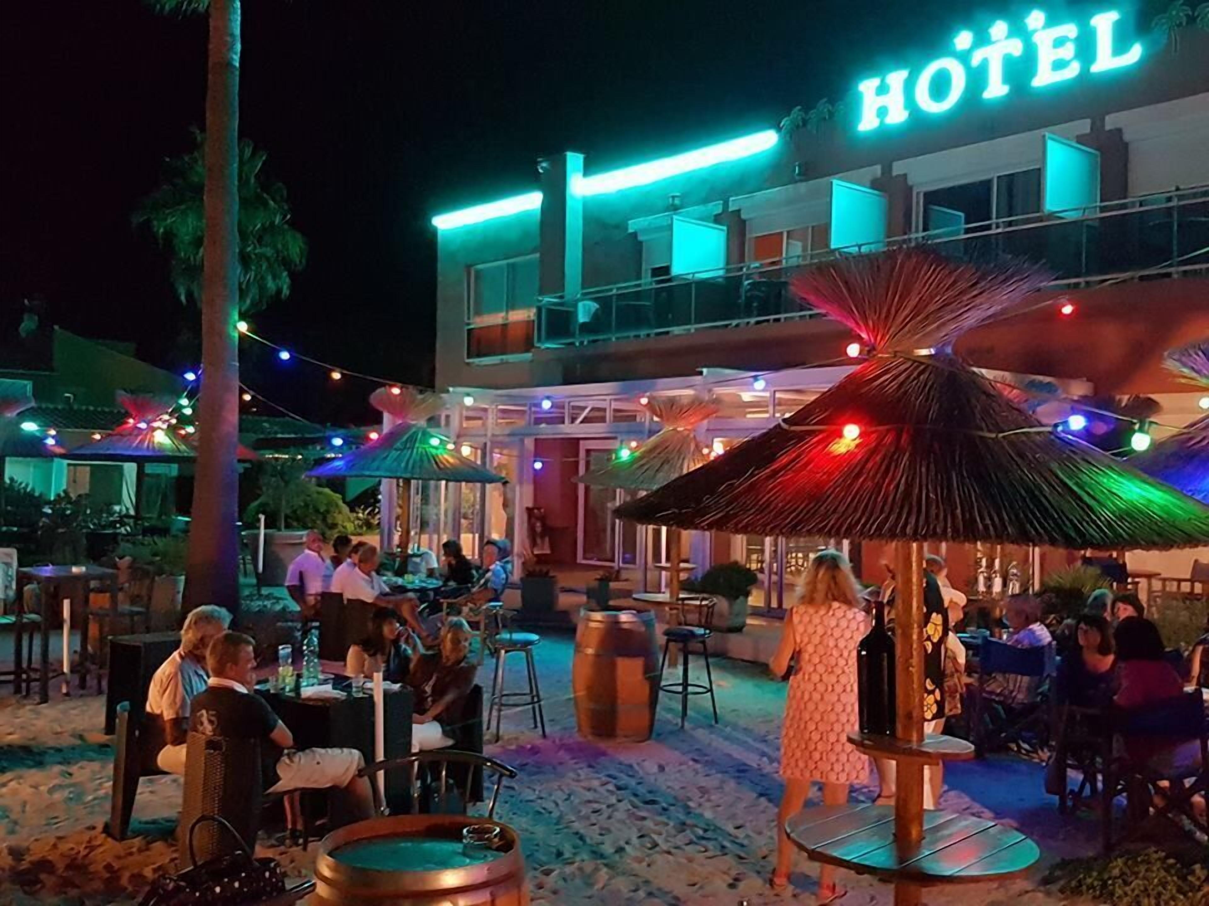 Un hôtel doté d’une terrasse avec des parasols, d’une piscine et d’une enseigne indiquant son nom.
