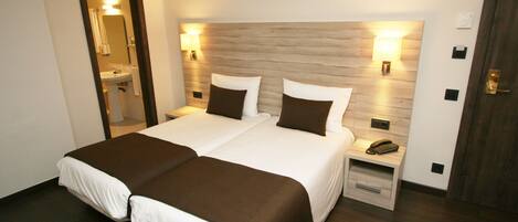 A double bed with two pillows, a bedside table with a phone, and a wall-mounted lamp.