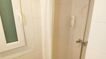 Um espaço de chuveiro pequeno e fechado, com porta de vidro, uma toalha branca pendurada na parede e um vaso sanitário com dispensador de papel.