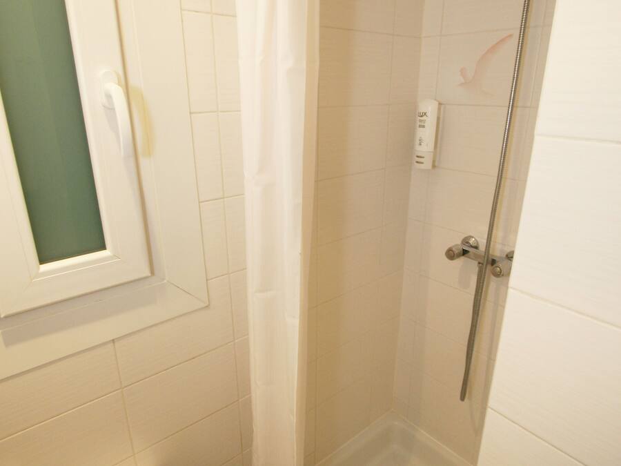 Um espaço de chuveiro pequeno e fechado, com porta de vidro, uma toalha branca pendurada na parede e um vaso sanitário com dispensador de papel.