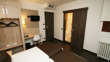 Habitación de hotel con cama, escritorio, silla, armario, televisor y puerta corredera que da al baño.