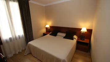 A hotel room with a large bed, two bedside tables with lamps, a wooden headboard, and a window with curtains.