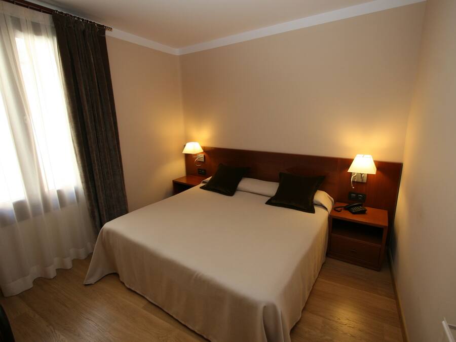 A hotel room with a large bed, two bedside tables with lamps, a wooden headboard, and a window with curtains.