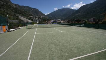 Un campo da tennis con una rete, circondato da montagne e edifici.
