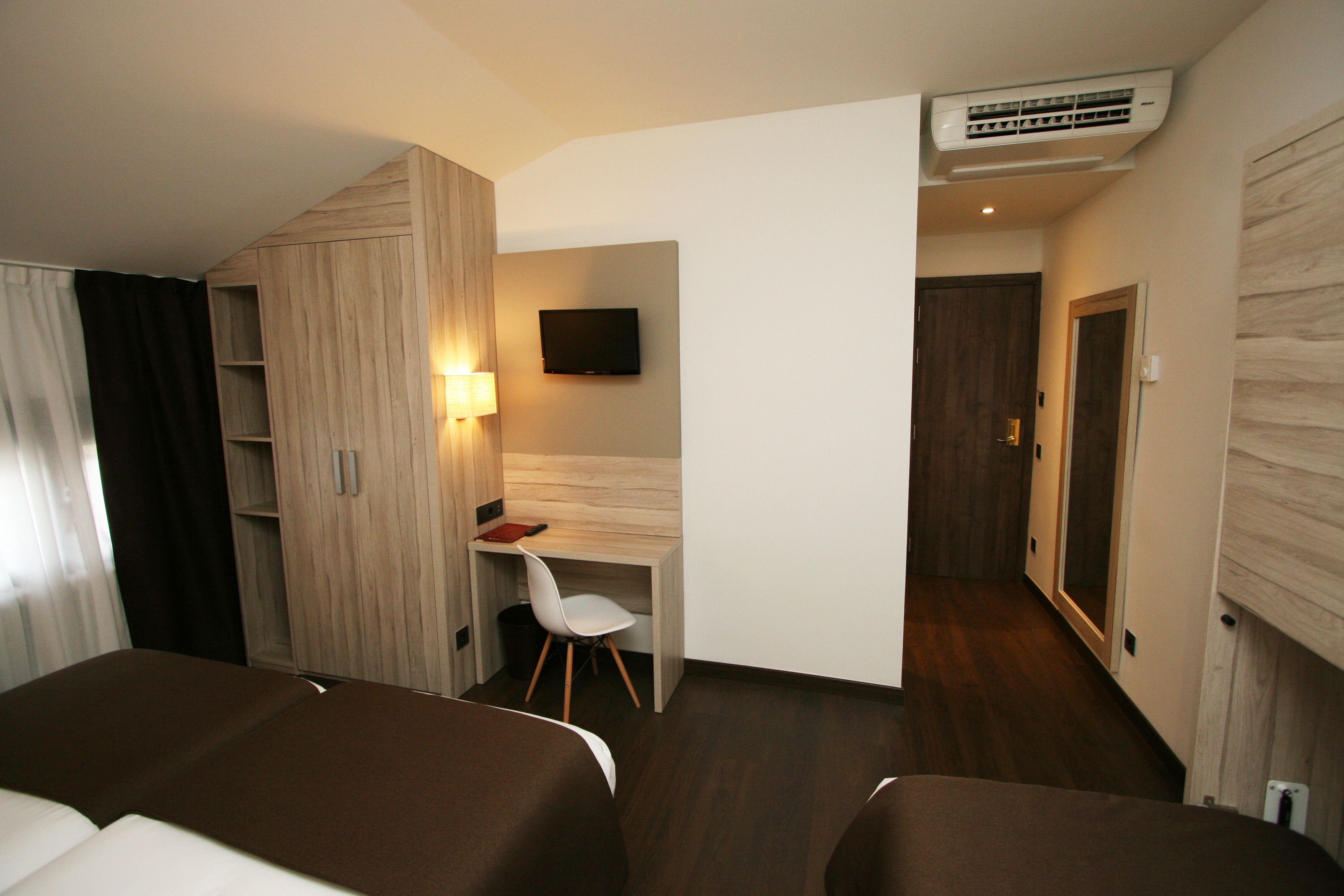 Una habitación de hotel con cama, escritorio, silla, televisor y aire acondicionado.