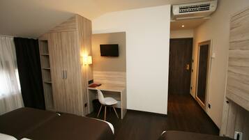 Una habitación de hotel con cama, escritorio, silla, televisor y aire acondicionado.