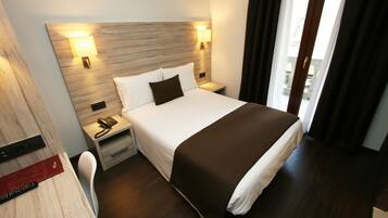 A hotel room with a large bed, two bedside tables with lamps, a desk with a chair, and a view of the outdoors through a window.